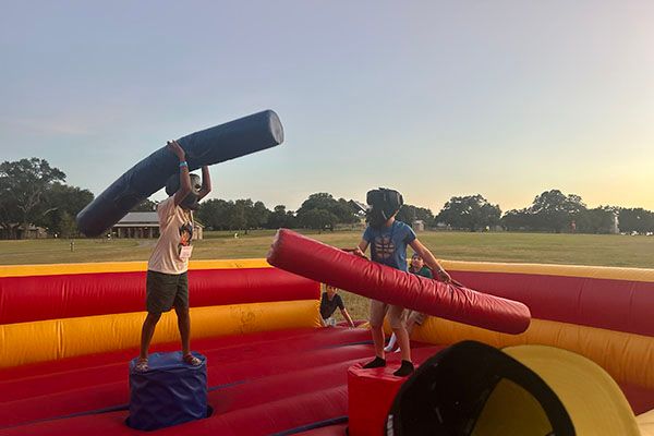 Campers play with pugil sticks on an inflated court in the twilight.